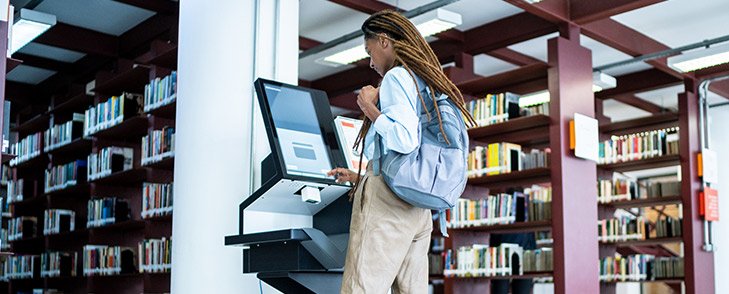 A student checks out a book using a computer in a library.
