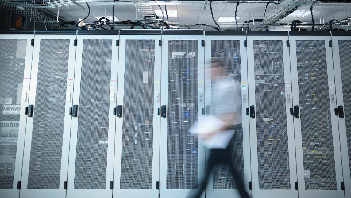 A blurred figure walks past rows of servers housed in cabinets.