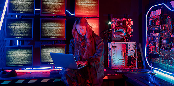A person with a laptop in a brightly lit server room.